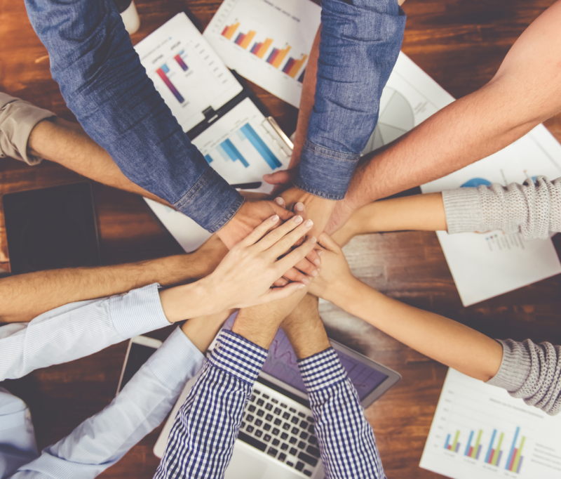 A group of individual's hands overlapping each other over a work table.